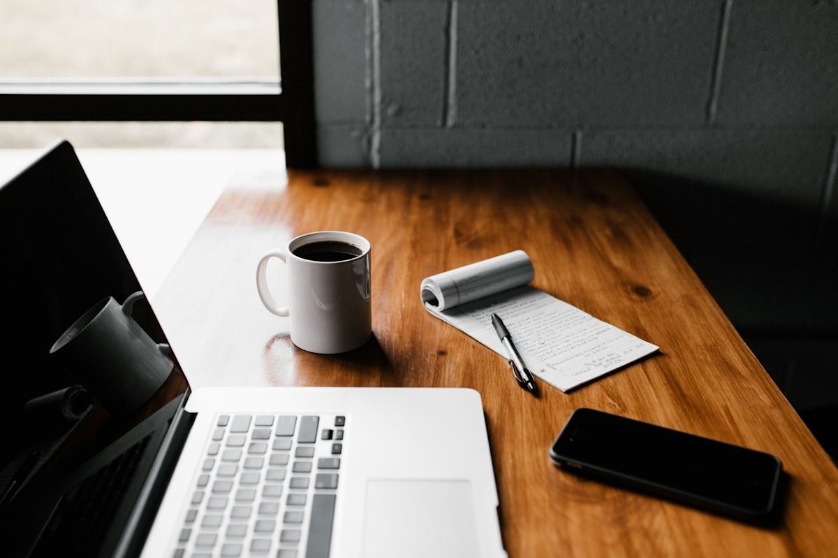 Portátil, taza de café y cuaderno con anotaciones sobre una mesa de madera