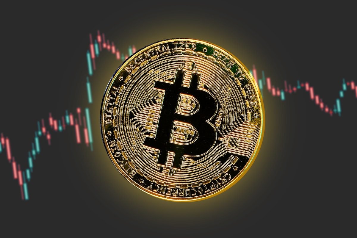 Moneda física de Bitcoin apoyada sobre una pantalla con un gráfico de cotización