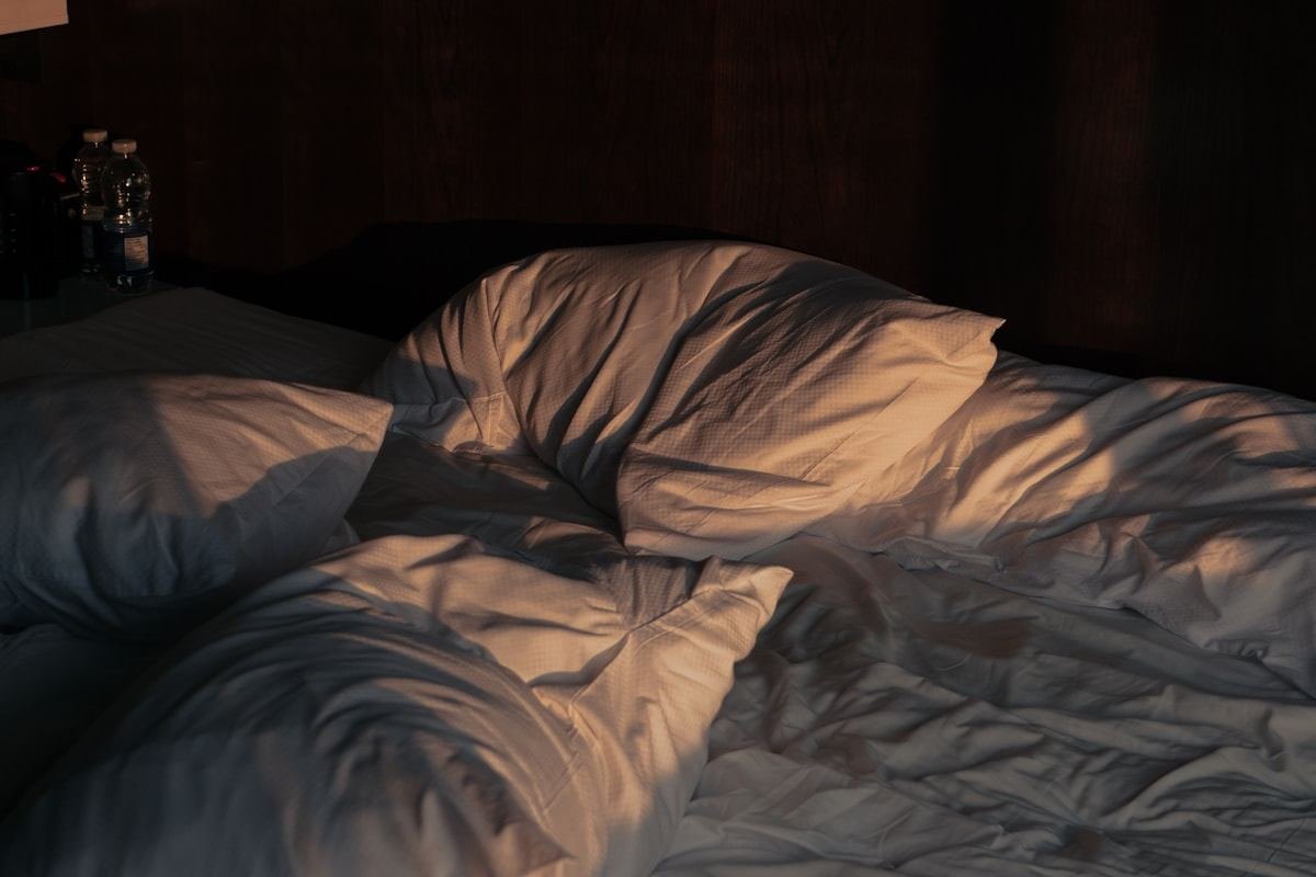Cama deshecha con sábanas claras iluminada por la luz de la mañana