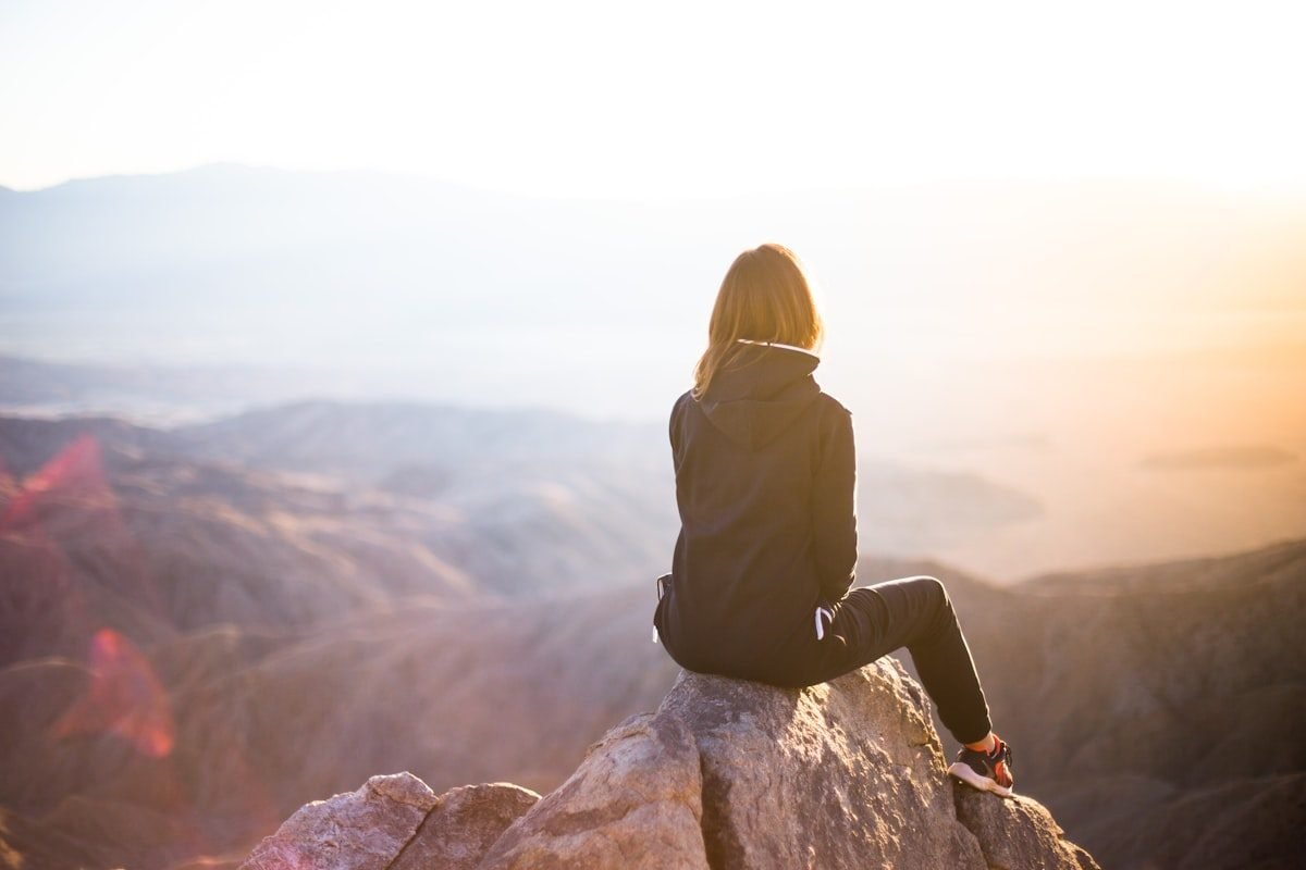 Persona sentada sobre una roca contemplando un valle montañoso con la luz dorada del amanecer