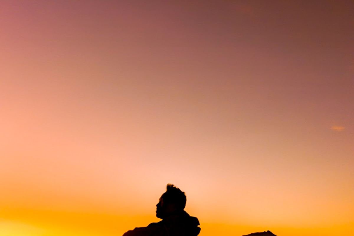 Silueta de una persona en la cima de una montaña al atardecer
